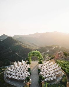 an outdoor ceremony setup with white chairs and greenery in the foreground, surrounded by mountains