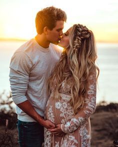 a man and woman kissing while the sun is setting over the ocean in the background