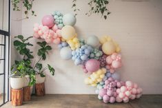 balloons are arranged in the shape of a letter on a wall next to potted plants