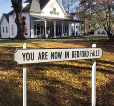 a sign that says you are now in bedford falls on the front lawn of a large white house