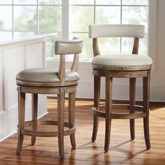 two wooden stools with white upholstered seats in front of a large window