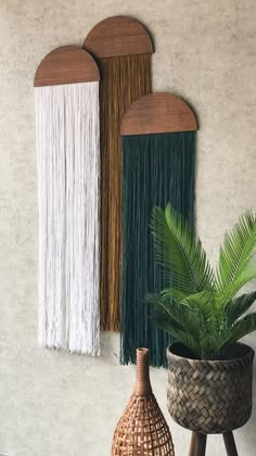 two wall hangings with different colors and designs on the wall next to a potted plant