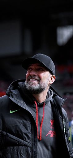 a man wearing a black jacket and hat standing in front of a crowd at a sporting event