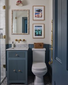 a white toilet sitting next to a blue sink in a bathroom under a framed mirror