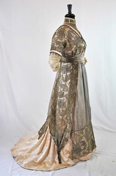 "EDWARDIAN AESTHETIC VELVET AND METALLIC LACE TRAINED GOWN, 1905 - 1910 One piece in construction, high net lace standing collar, V-shaped front and back with beadwork, metallic net lace over satin, velvet sash at waist adorned with metallic floral appliques. Double short sleeves with gold metallic lace netting, beaded dangles and ending with tiered valenciennes lace.  Streamer panels drapes its sides with metallic tassels. Nine fabric covered stays. Extensive hook and loop closures.  Chiffon inserts front and back. Satin and cotton lining. Unlabeled. APPROXIMATE MEASUREMENTS: Bust 37\" Waist 29\" Sleeve length 18\" Across back shoulder to shoulder 12\" Front shoulder to waist 17\" Front Shoulder to Hem line 53\" Back Shoulder to Hem line 61\". ERA: 1905 to 1910. CONDITION: In very good co Edwardian Aesthetic, Fashion 1910, Augusta Auctions, Satin Evening Gown, 1910s Fashion, Peacock Dress, Edwardian Dress, Old Dresses, Retro Mode