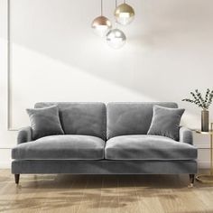 a gray couch sitting on top of a hard wood floor next to a vase filled with flowers