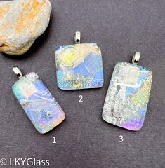 three pendants with different designs on them sitting next to a rock and some rocks