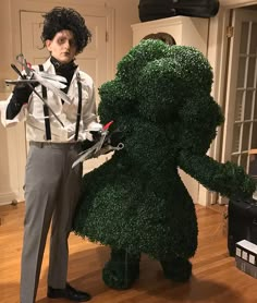 a man dressed in costume standing next to a fake dog made out of grass with scissors