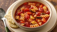 a bowl of pasta soup with bread on the side