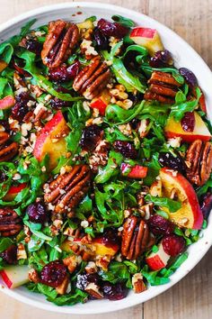 a salad with apples, cranberries and pecans in a white bowl on a wooden table