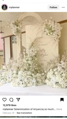 white flowers and greenery are arranged on a table in front of a wedding sign