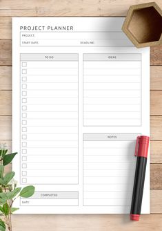 a printable project planner on top of a wooden table next to a pen and potted plant