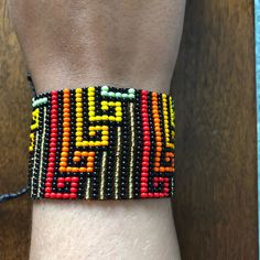 a hand made beaded bracelet on someone's wrist with an orange, yellow and green design