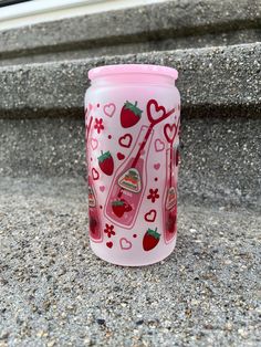 a pink glass cup with strawberries and hearts on it sitting on the ground next to some steps