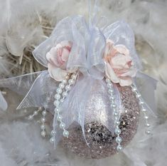 a silver ornament with flowers and pearls hanging from it's side on some feathers