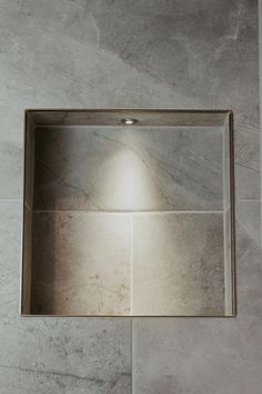 a square mirror mounted on the wall above a sink in a tiled room with grey walls