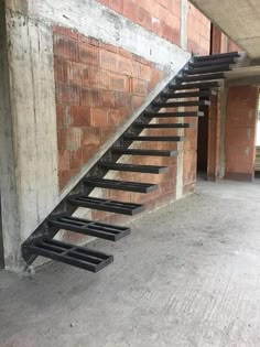 a set of black metal stairs in front of a brick wall and concrete flooring