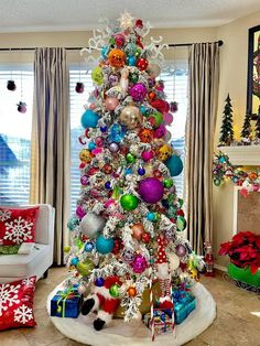 a brightly colored christmas tree in a living room decorated with ornaments and presents for the holiday season