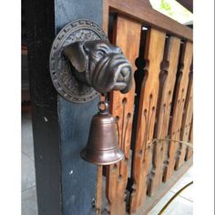 a metal dog head mounted to the side of a wooden gate with a bell on it