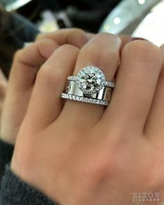 a woman's hand holding a diamond ring and two wedding bands on her fingers