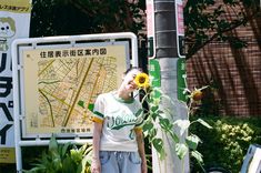 a man standing next to a tree with a sunflower in his hand and a map behind him