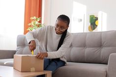 a woman sitting on a couch opening a box