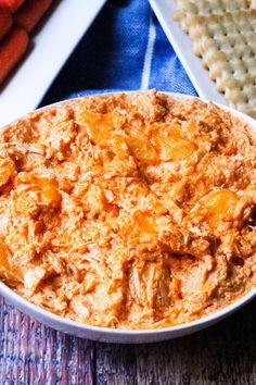 a bowl of food sitting on top of a table next to carrots and crackers