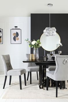 a dining room table with chairs and pictures on the wall behind it, along with vases filled with flowers