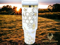 the sun is setting over a field with flowers and bees on it, as well as an insulated tumble cup