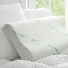 a close up of a pillow on a bed with white sheets and pillows in front of a window