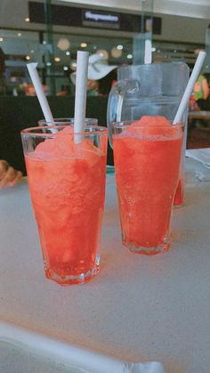 two glasses filled with watermelon drink sitting on top of a white table next to each other