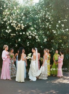 a group of women standing next to each other in front of trees and white flowers