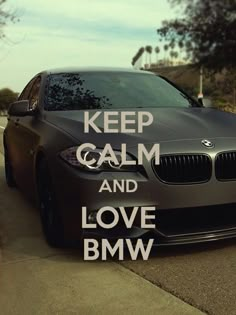 a black car parked on the side of a road next to a sign that says keep calm and love bmw