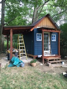 a small blue shed with a ladder next to it in the grass and some trees