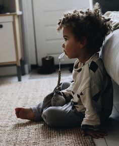 a little boy sitting on the floor with a stuffed animal in his mouth