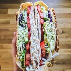 a person holding up a sandwich with meat and veggies on it in front of a wooden floor