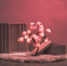 a small tree with pink flowers in a vase on a fur covered table next to a box