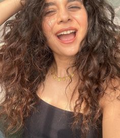 a woman with curly hair smiling and holding her head