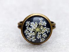 Beautiful and individual ring with a real dried flower.The white flower was poured in resin and is therefore protected. The black background the flower is especially nicely.Since it is a real flower, each piece is unique and may vary slightly from the photo.The ring is nickel and lead free. The flower has a stone through Esser of 14 mm /0,55 zoll. The ring rail is adjustable in size, so the ring finger size can be customized and is also suitable as a gift.The ring is beautiful & packed safel Round Floral Print Jewelry Gift, Floral Print Round Jewelry Gift, Floral Print Round Jewelry For Gifts, Round Floral Print Jewelry For Gift, Black Pressed Flowers Jewelry Gift, Black Flower-shaped Rings For Gifts, Black Flower Shaped Ring For Gifts, Black Flower Shaped Rings For Gift, White Flower Ring