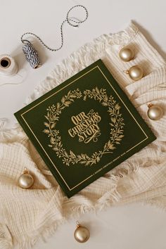 a green book sitting on top of a white blanket next to some gold ornaments and twine