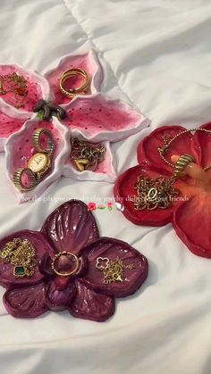 three flower shaped trays with rings and jewelry in them sitting on a white sheet