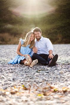 a man and woman are sitting on the ground in front of some rocks, smiling at each other