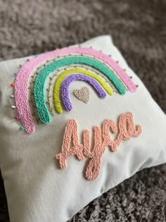 a white pillow with embroidered words and a rainbow on the back that says, happy