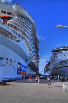 two cruise ships are docked at the dock with people walking around them and one is in the foreground