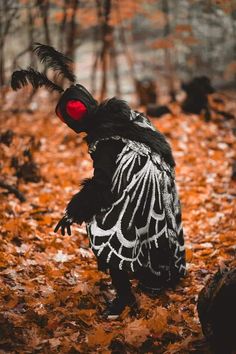 a person dressed up as a bird with red eyes and black feathers in the woods