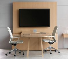 a table with two chairs and a television mounted on the wall above it in an office setting