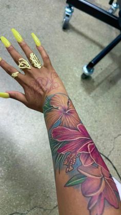 a woman's arm with yellow nail polish and flower tattoo on the left hand