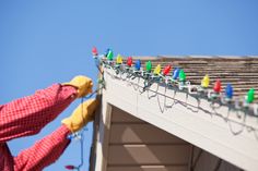 a man in yellow gloves working on a roof with christmas lights attached to the gutter