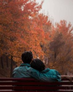 two people sitting on a red bench in the fall with their arms around each other