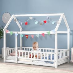 a baby sitting in a white crib next to a wall with bunting flags